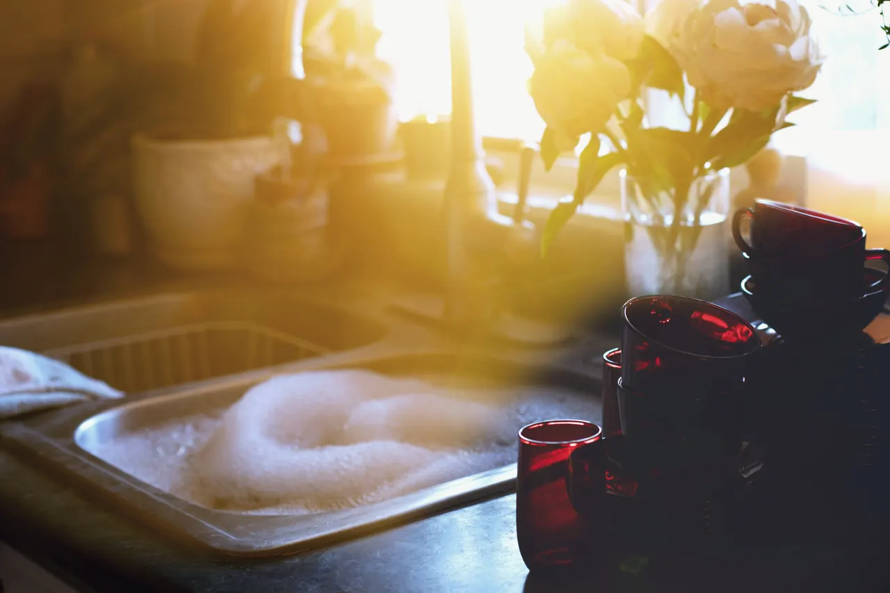 A kitchen sink full of suds in low golden sunlight.