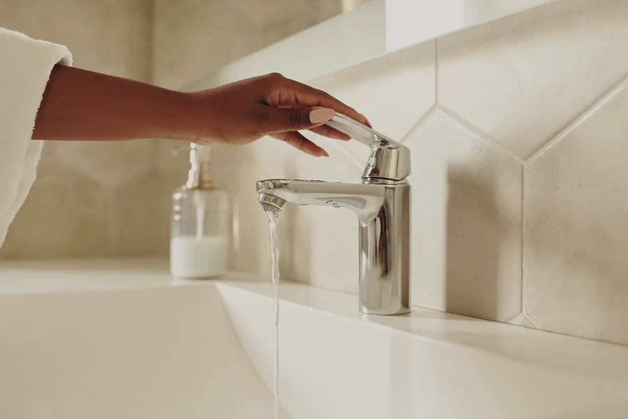 A hand turning on a chrome lever faucet over a white basin.