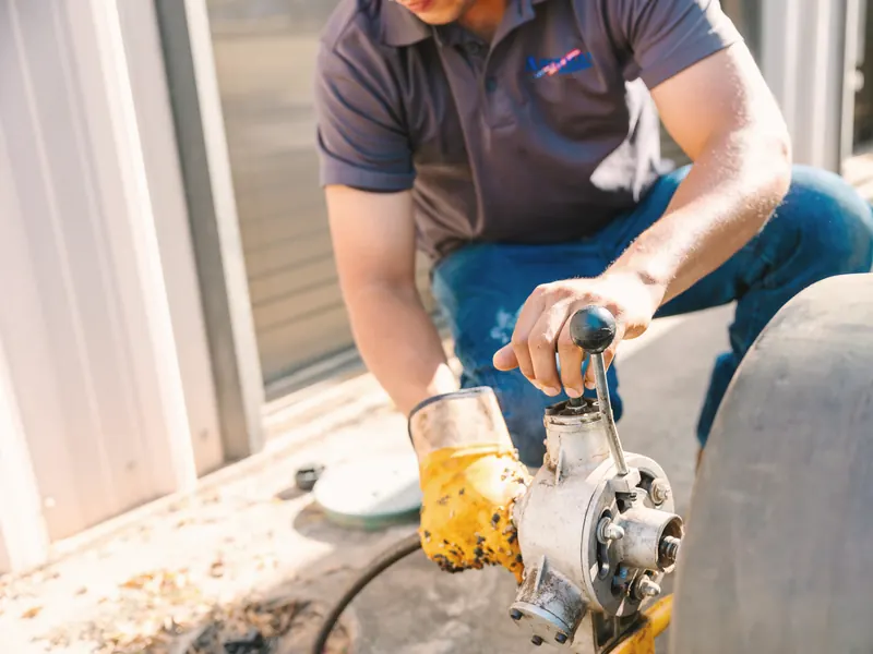 A technician in work gloves runs a drain-cleaning machine at a doorway.