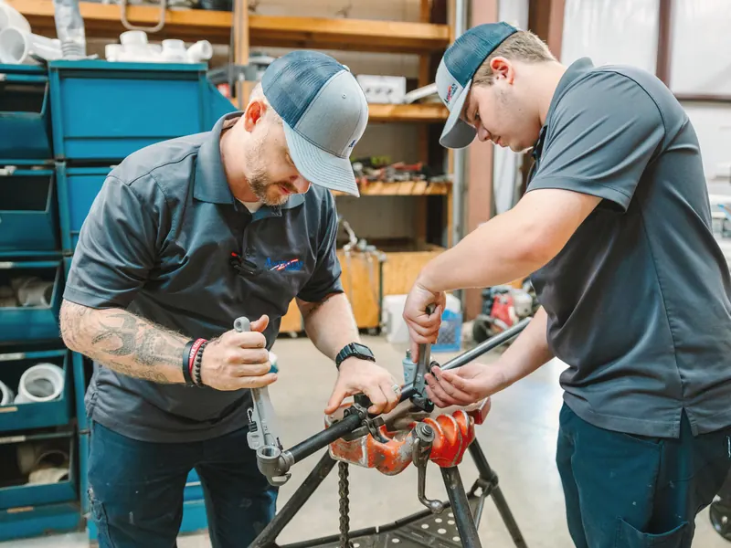 Two technicians thread a length of pipe on a stand in the company shop.