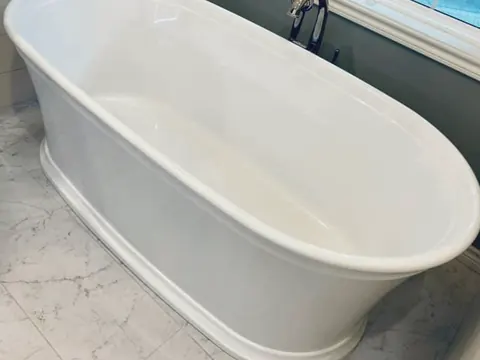 A freestanding white tub with a floor-mounted faucet below a window.