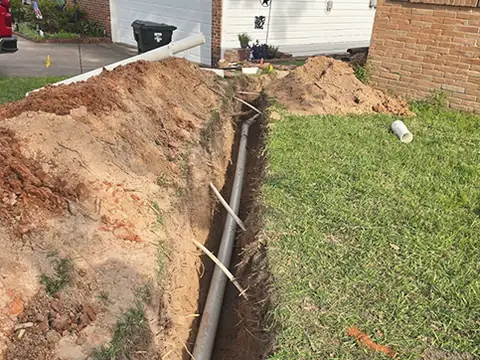 A long trench across a front lawn with a new pipe laid in it.