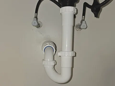 A new white PVC P-trap and shut-off valves under a sink.